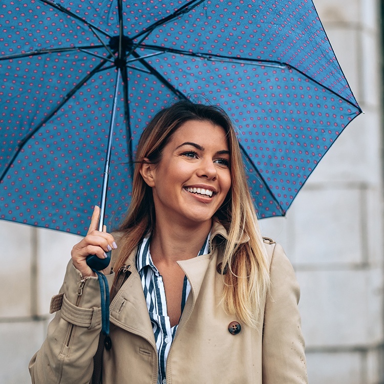Woman with dental insurance smiling and holding an umbrella