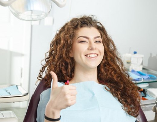young woman smiling and giving thumbs up in dental chair 