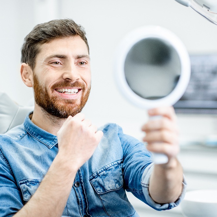Male dental patient checking smile in handheld mirror