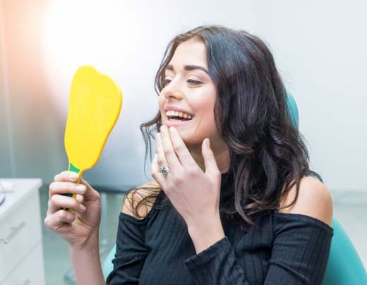 woman admiring her smile in a mirror after getting a dental crown 