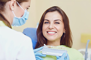 A younger woman smiles as a dentist determine the appropriate shade for her customized dental crown that will sit on top of her dental implant