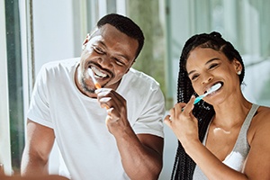a couple smiling while brushing their teeth together