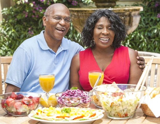 couple sitting at a table outside with various foods and beverages