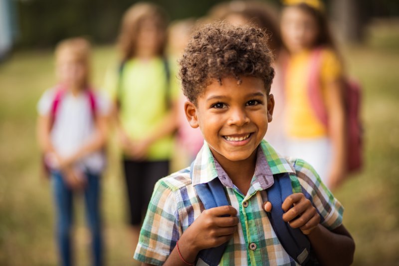 Child with backpack smiling with friends at school